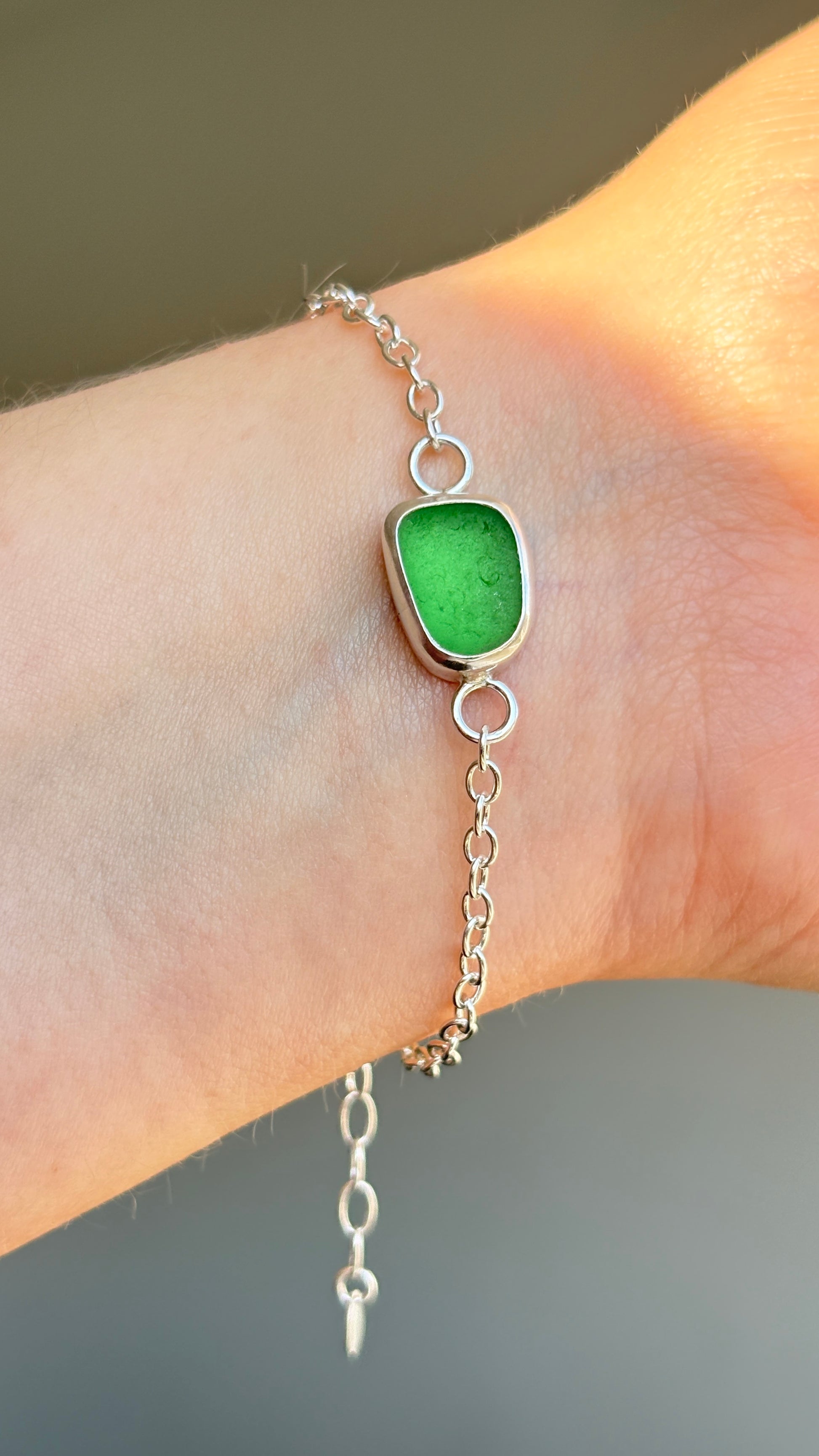 Green sea glass bracelet on a wrist with a neutral background